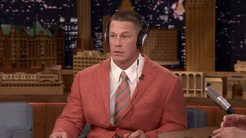 A moving gif of John Cena wearing headphones at a Jimmy Fallon show, vibing to the music